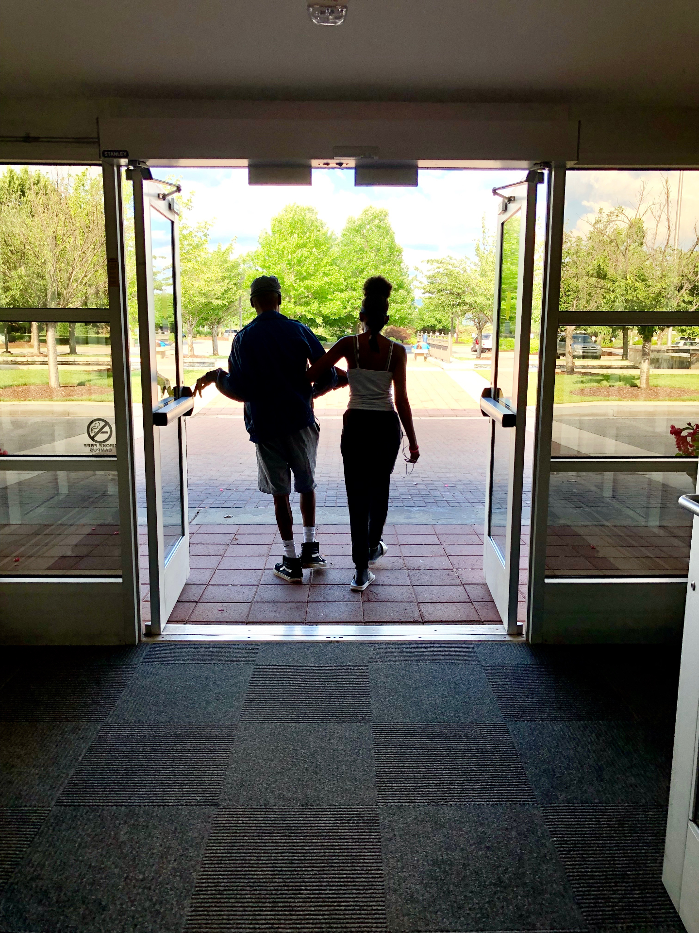 A father gently holding his young daughter's hand as they walk out of the hospital entrance toward the sunlight, symbolizing hope after treatment.